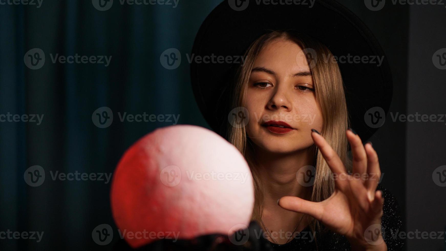 una adivina joven con un sombrero sostiene una bola mágica. foto