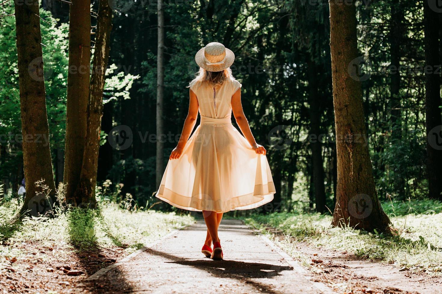 A young woman in a white dress and a straw hat walks through the woods photo