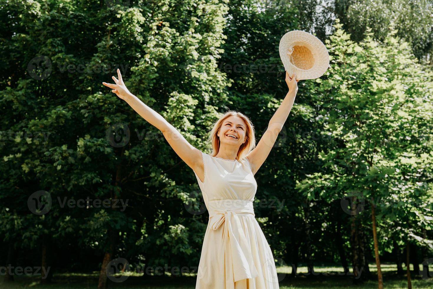 Hermosa joven con sombrero de paja y vestido blanco en un parque verde foto