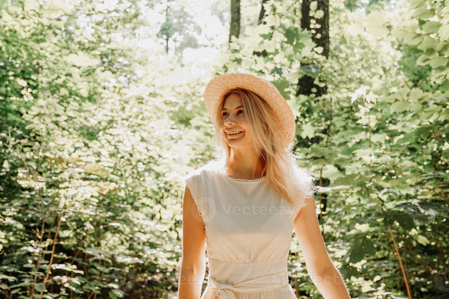 Hermosa joven con sombrero de paja y vestido blanco en un parque verde foto