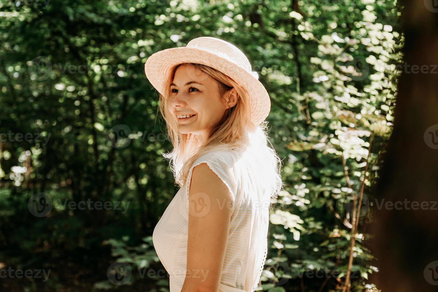 Hermosa joven con sombrero de paja y vestido blanco en un parque verde foto