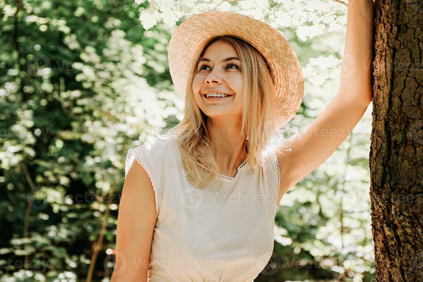 hermosa chica con un sombrero de paja y ropa elegante se encuentra cerca de un árbol foto