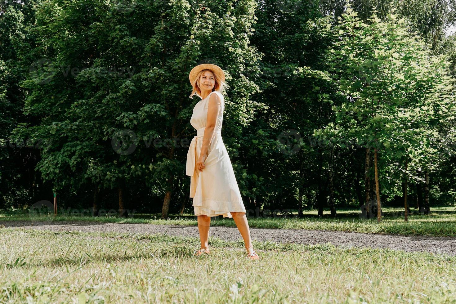 Hermosa joven con sombrero de paja y vestido blanco en un parque verde foto