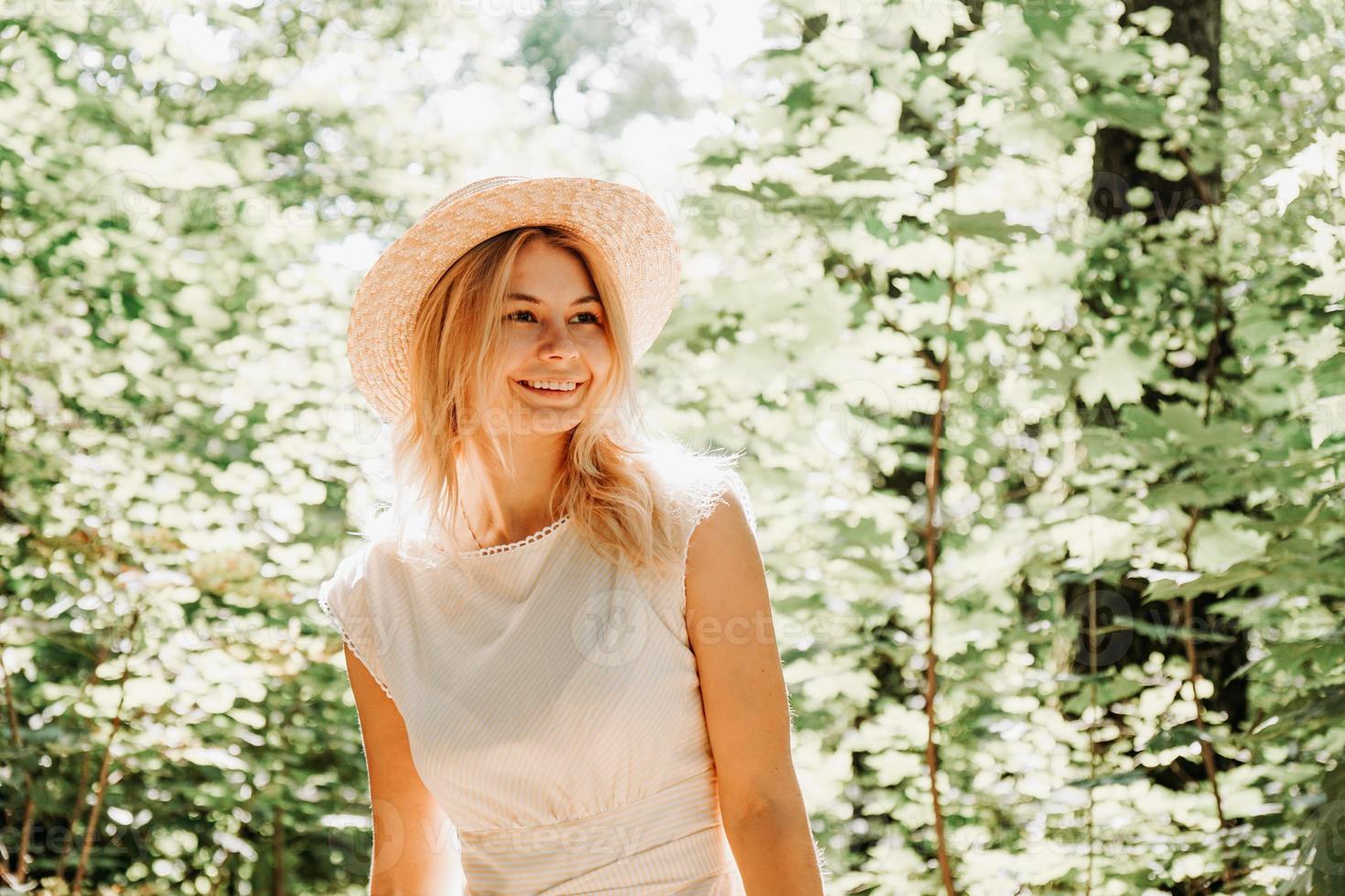 Hermosa joven con sombrero de paja y vestido blanco en un parque verde foto