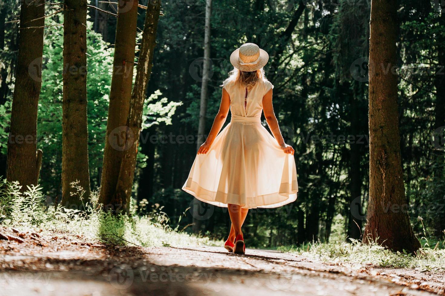 A young woman in a white dress and a straw hat walks through the woods photo