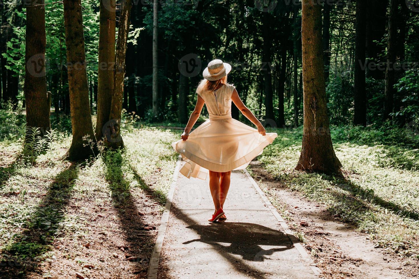 una mujer joven con un vestido blanco y un sombrero de paja camina por el bosque foto