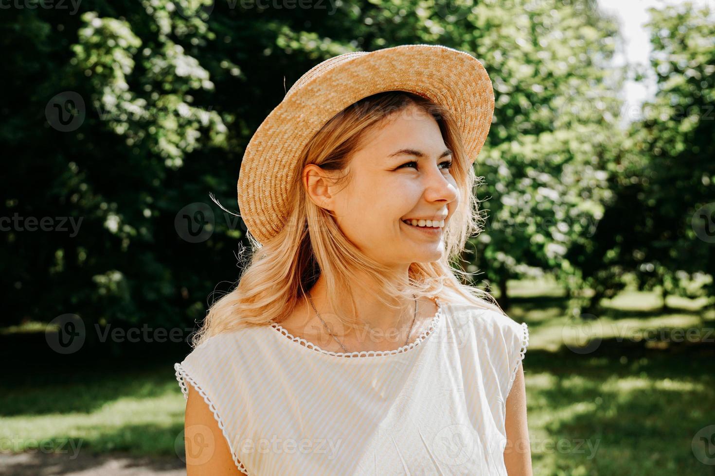 Hermosa joven con sombrero de paja y vestido blanco en un parque verde foto