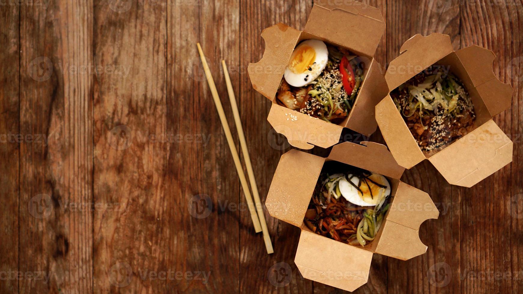 Chinese noodles with chicken in cardboard boxes on a wooden background photo