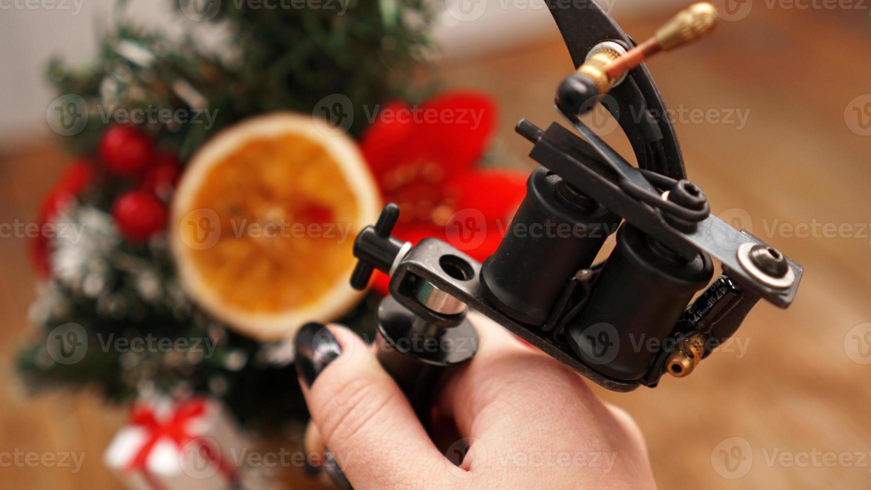 Female hand holding tattoo machine on blurred christmas tree photo