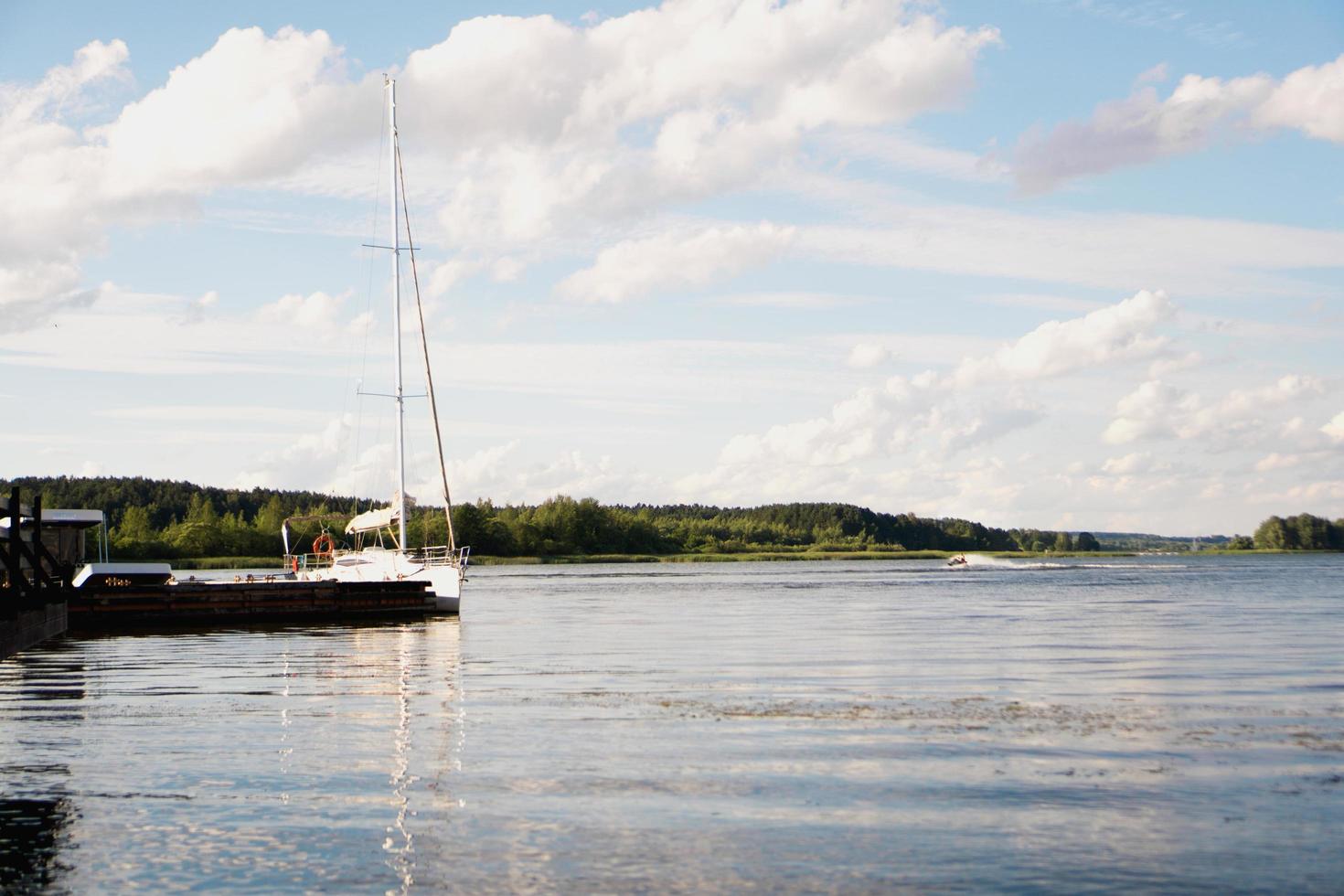 Yacht on blue peaceful lake on green forest and blue sky background photo