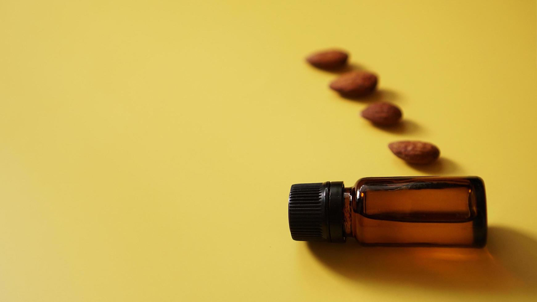 Bottle of almond oil and almonds on yellow background photo