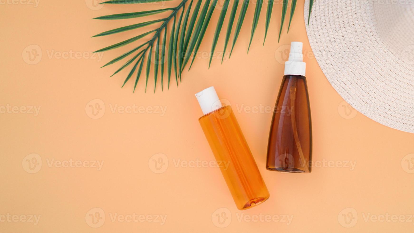 Sun cream, sun hat, lotion bottle on soft orange background photo