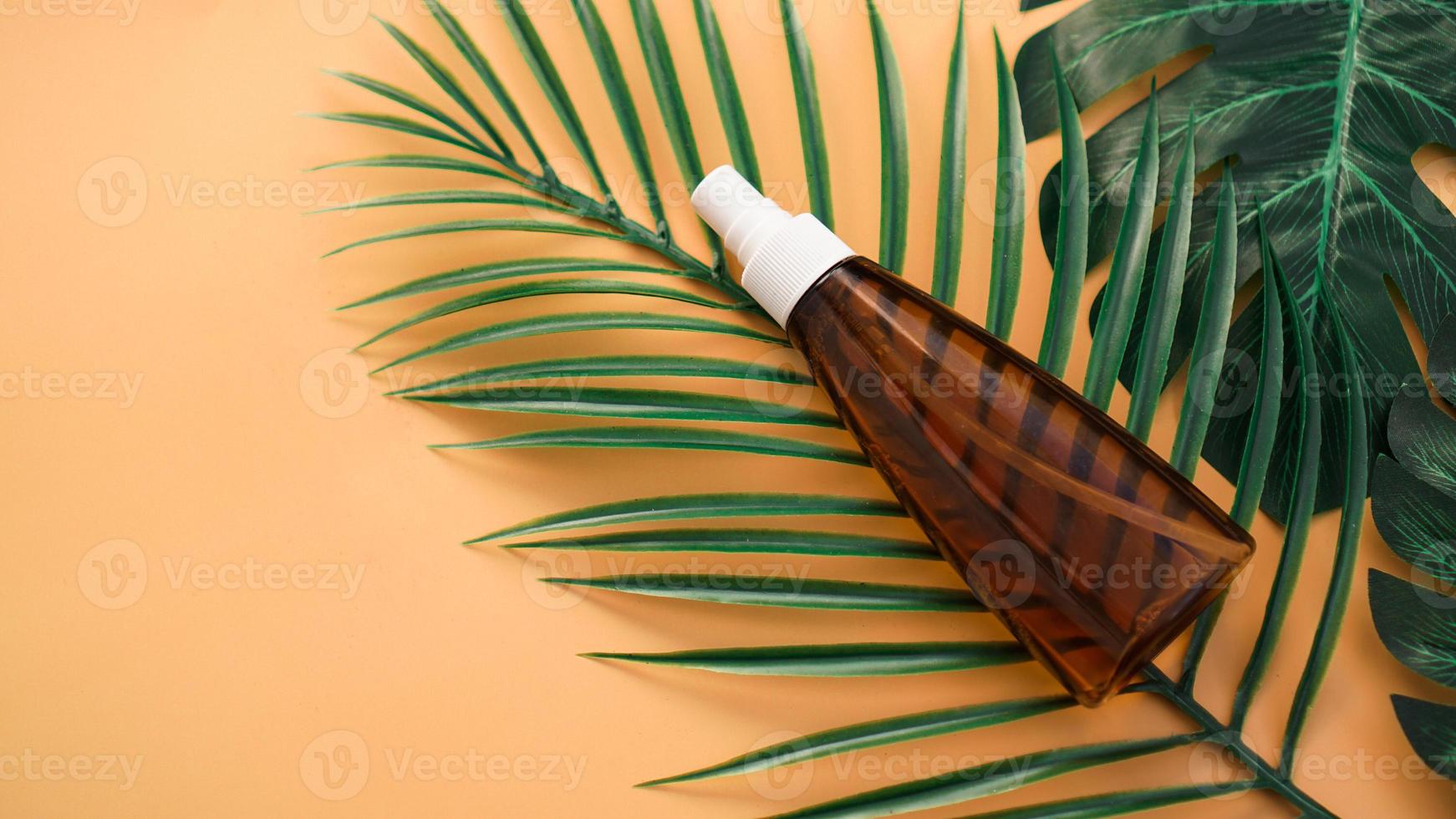 Botella de loción bronceadora sobre fondo con hojas tropicales foto