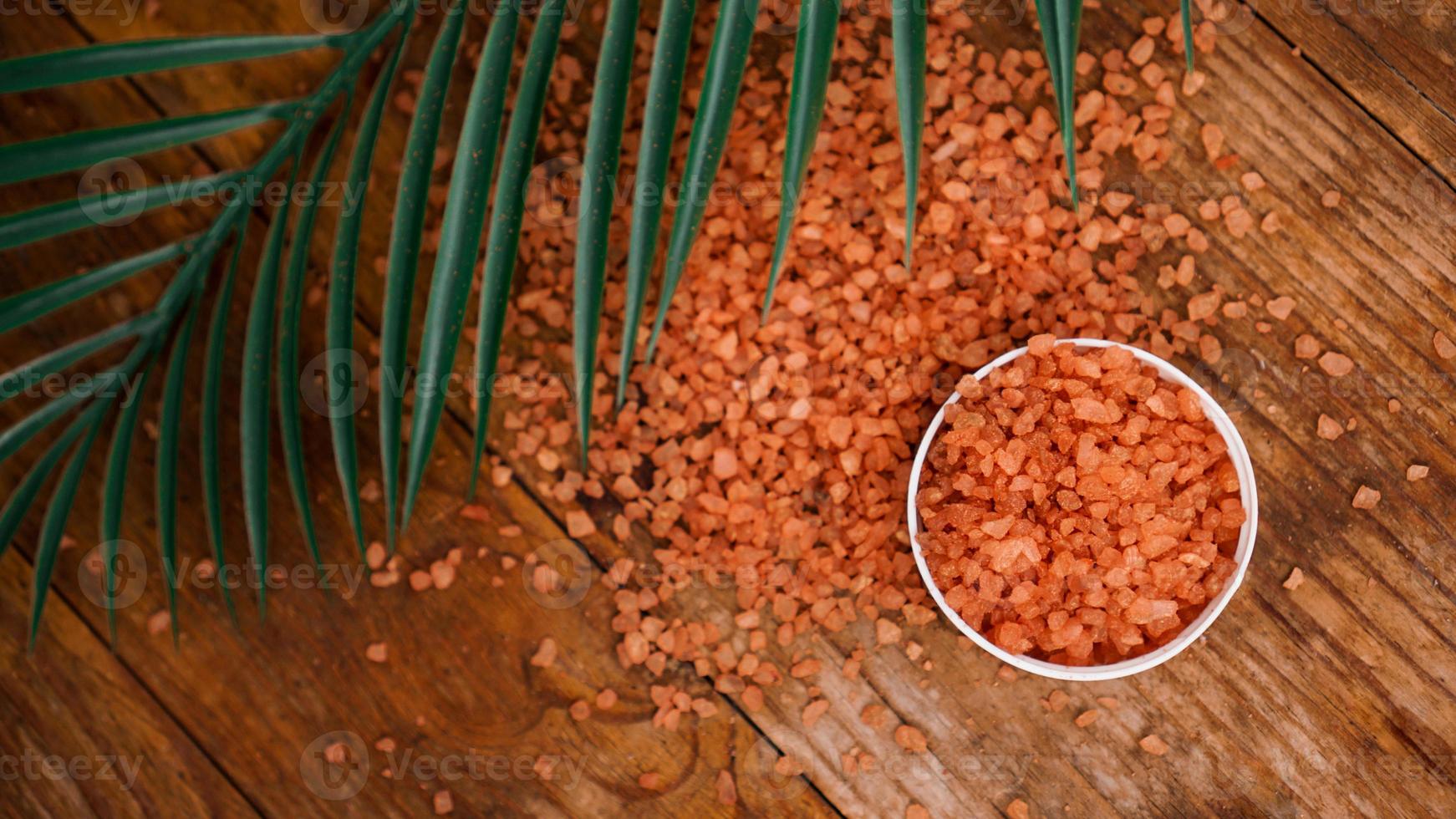 Orange sea salt on a wooden background. Tropical palm leaves photo