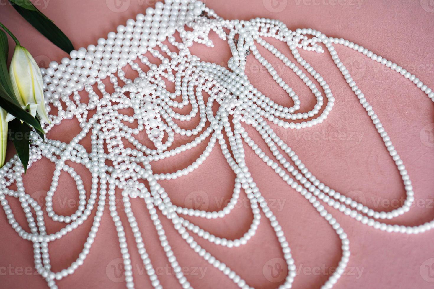 lirios blancos y un collar de perlas sobre un fondo rosa. foto