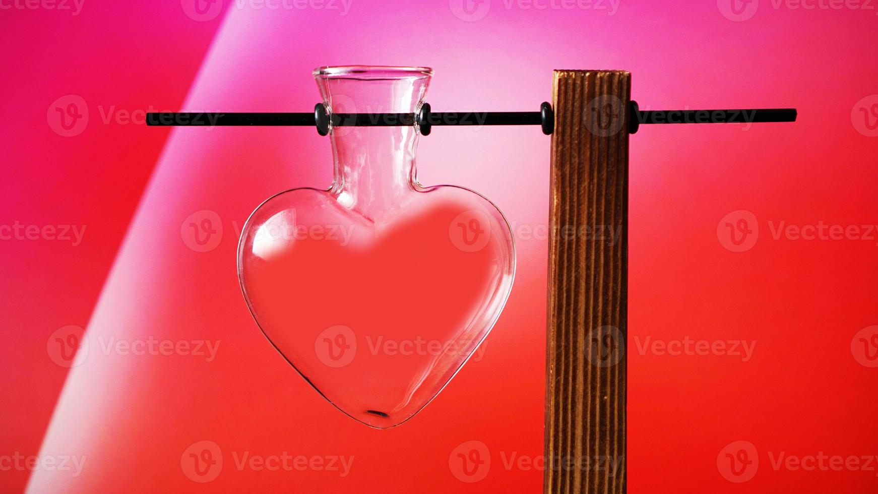 Frasco de vidrio en forma de corazón vacío sobre soporte de madera en rojo foto