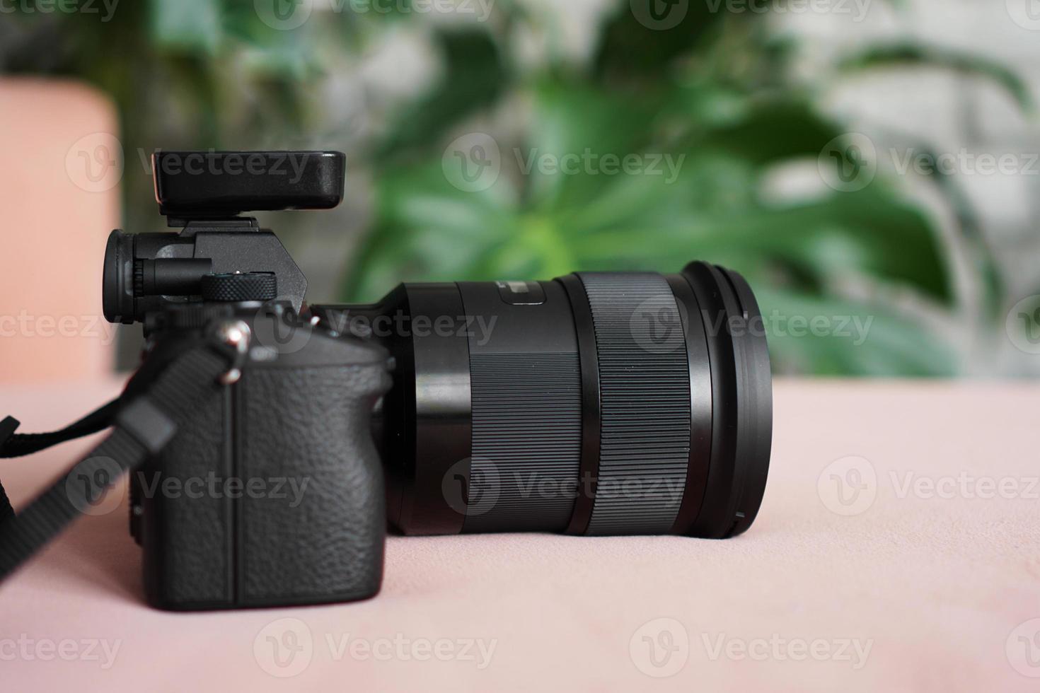 Black camera with a lens on a blurred background of green leaves. photo