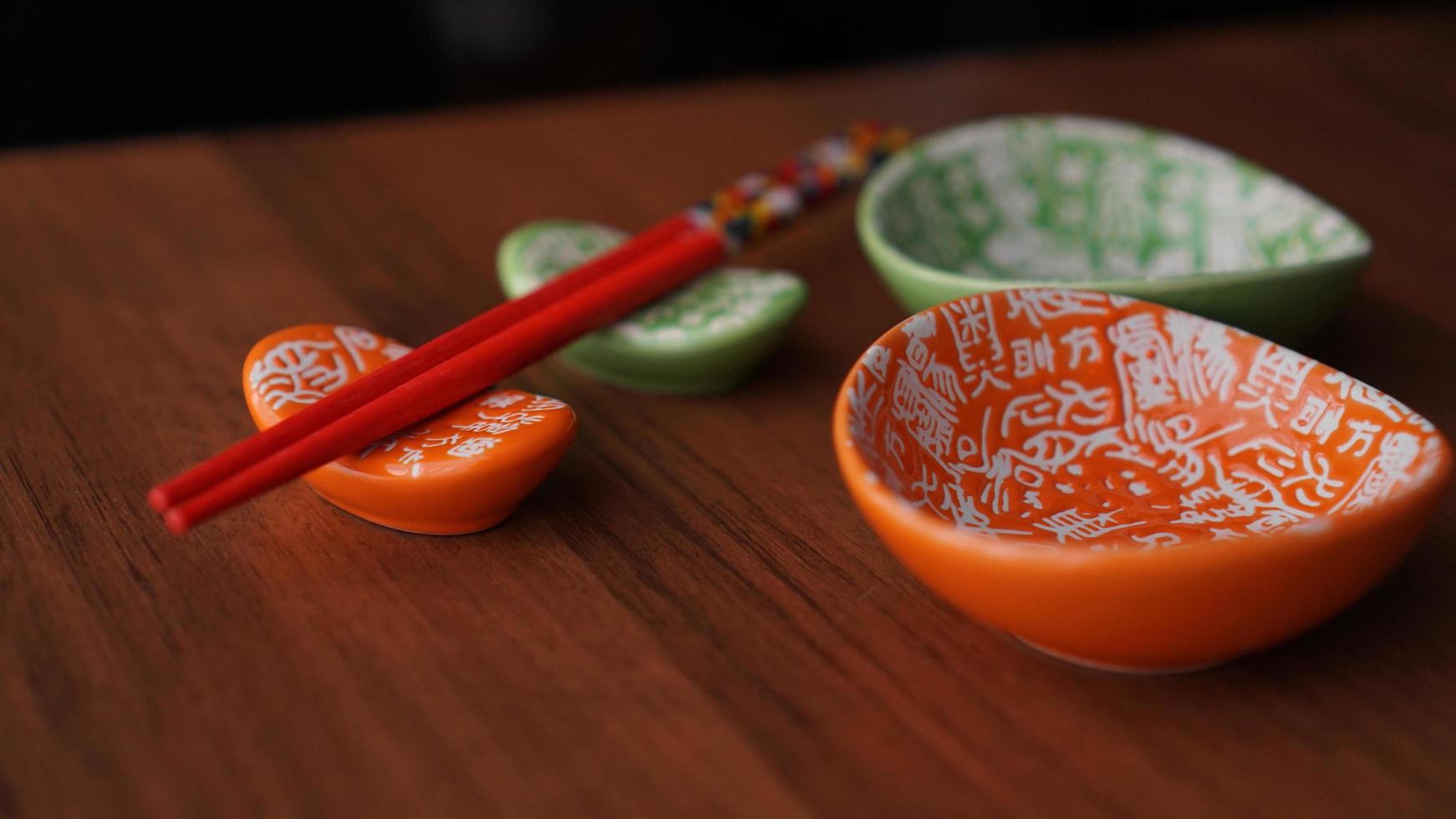 Set of ceramic dishes and red sushi sticks on wooden background photo