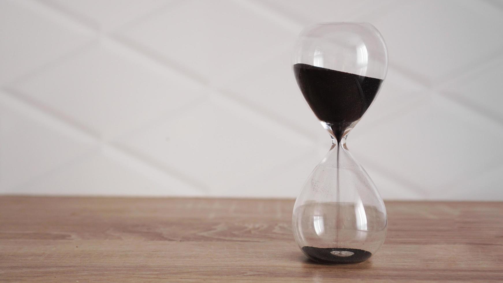 Crystal hourglass with black sand on wooden table photo