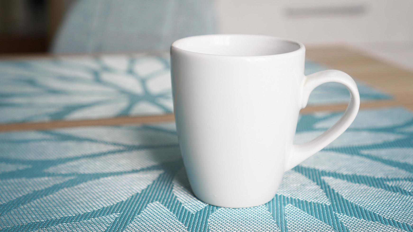 Clean white mug with handle stands on blue table photo