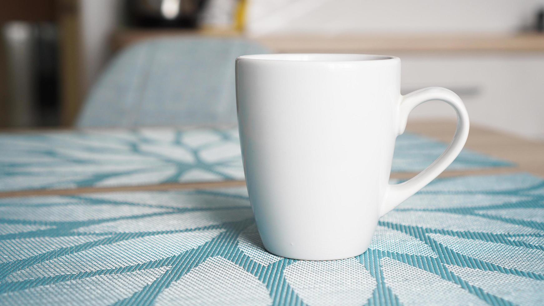 Clean white mug with handle stands on blue table photo