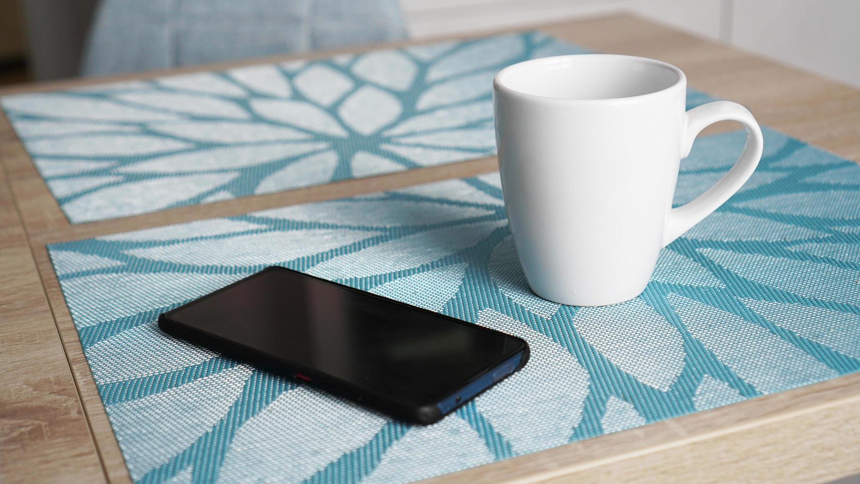 Clean white mug and smart phone on the table photo