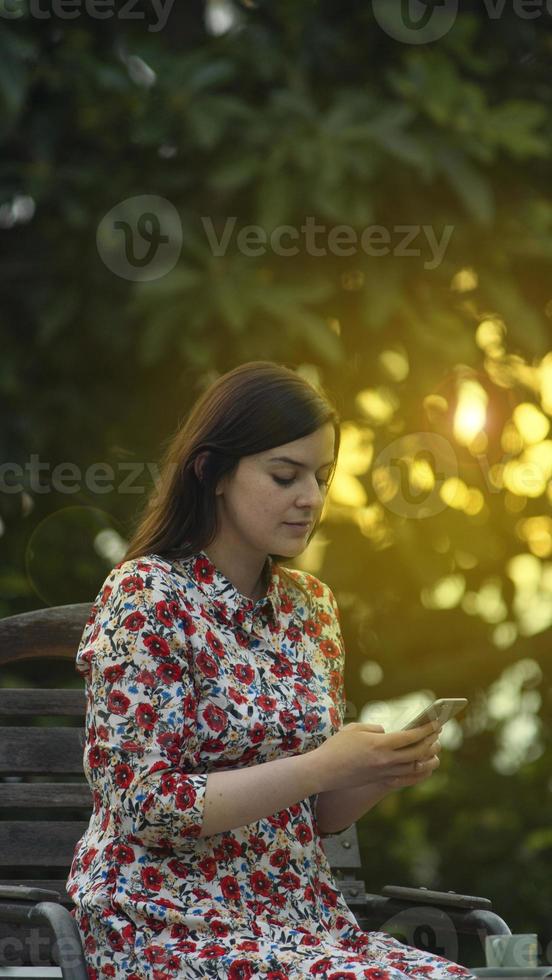 Belleza latina joven en vestido floral blanco leyendo en el teléfono inteligente foto