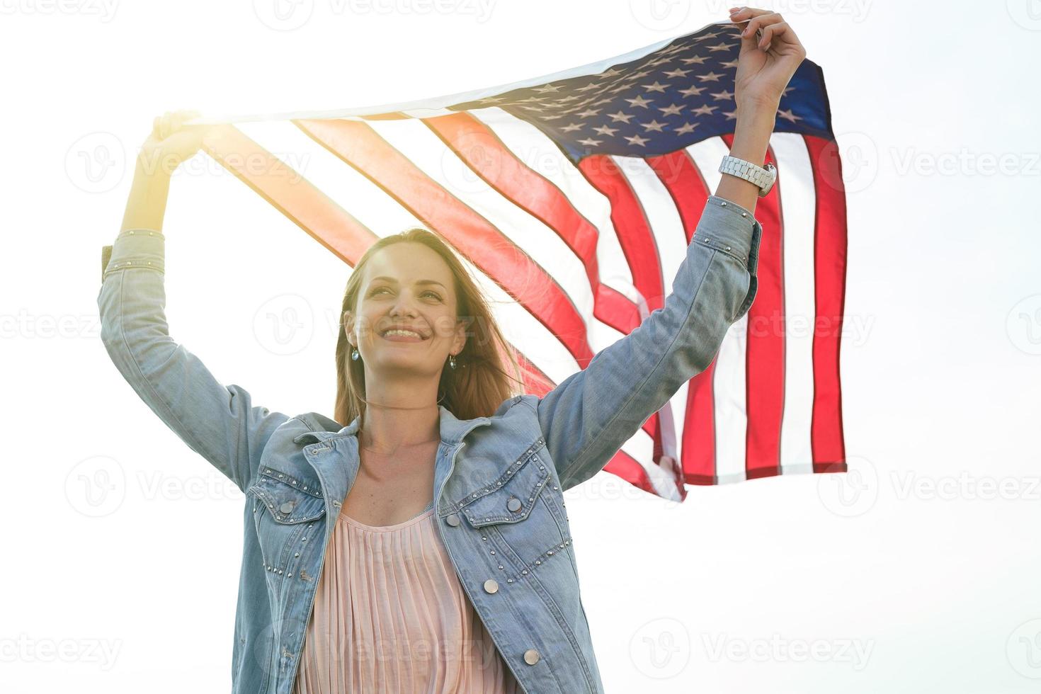 A girl in a coral dress and a denim jacket holds the flag of usa photo