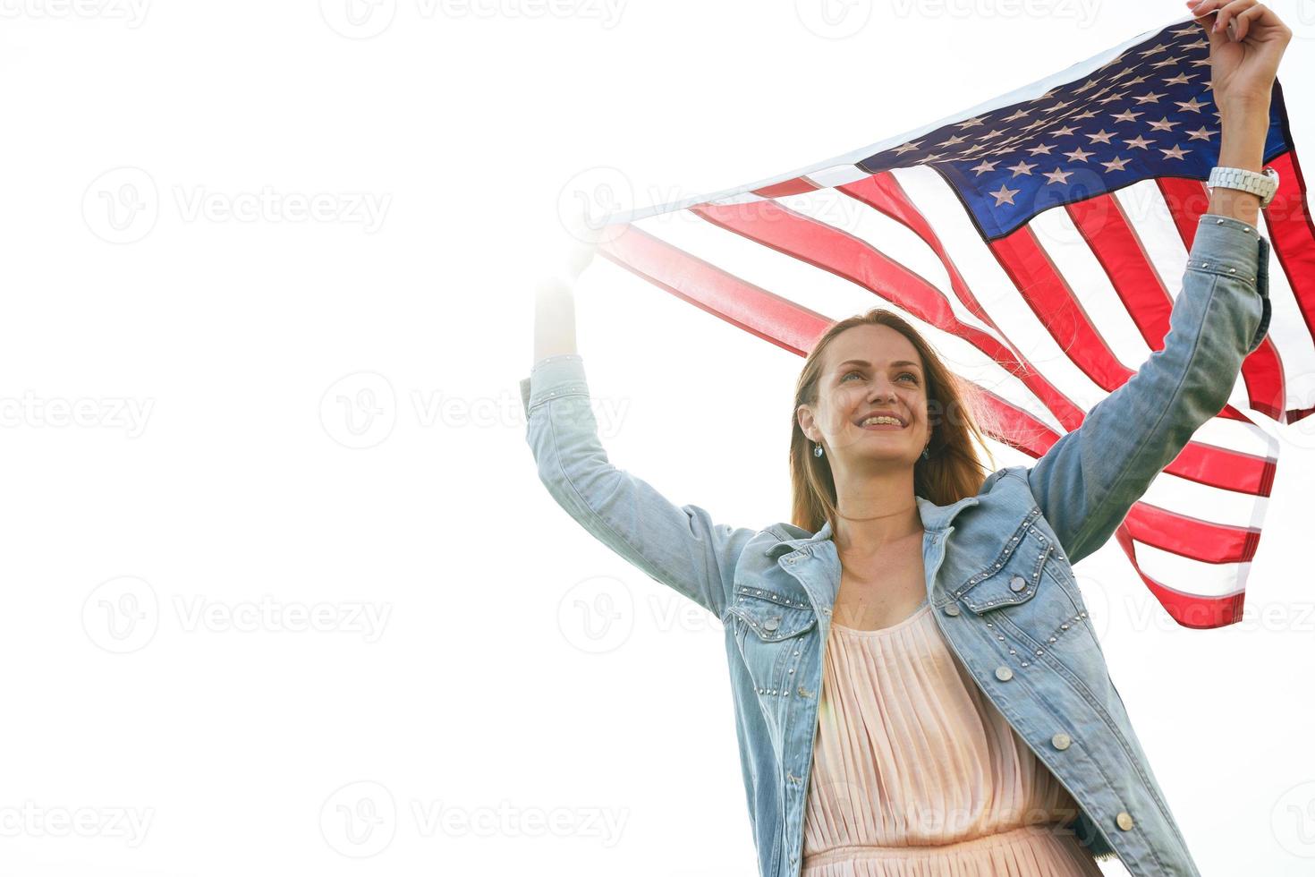 A girl in a coral dress and a denim jacket holds the flag of usa photo