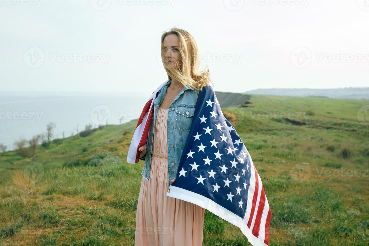 A girl in a coral dress and a denim jacket holds the flag of usa photo