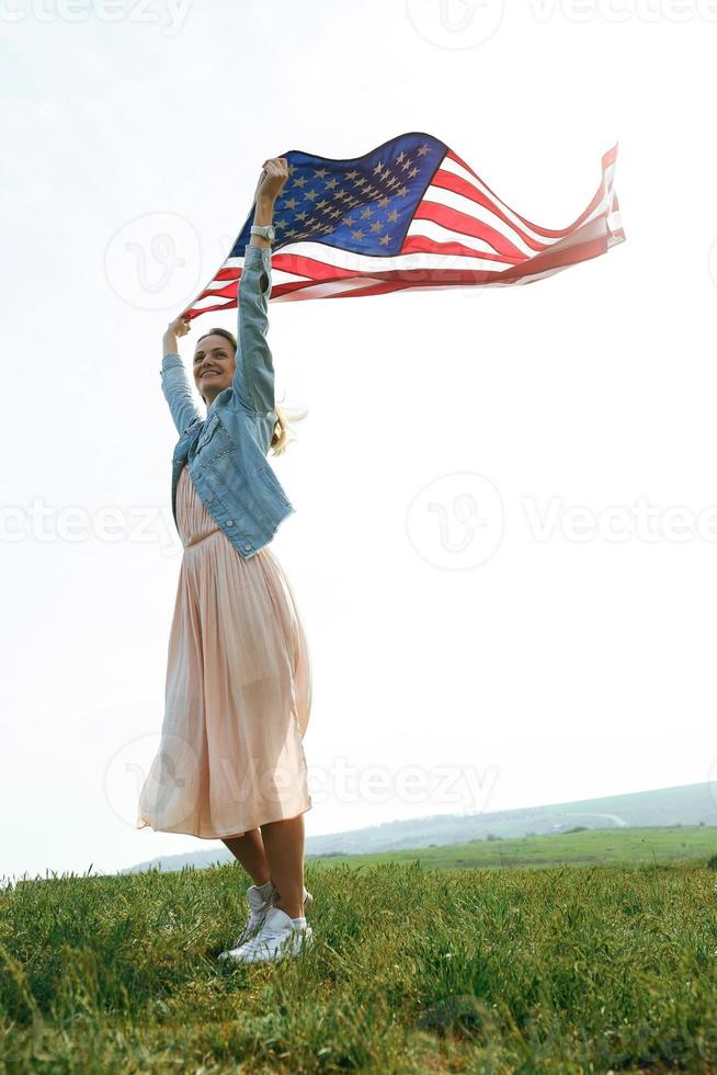 Una niña con un vestido coral y una chaqueta vaquera sostiene la bandera de EE. UU. foto