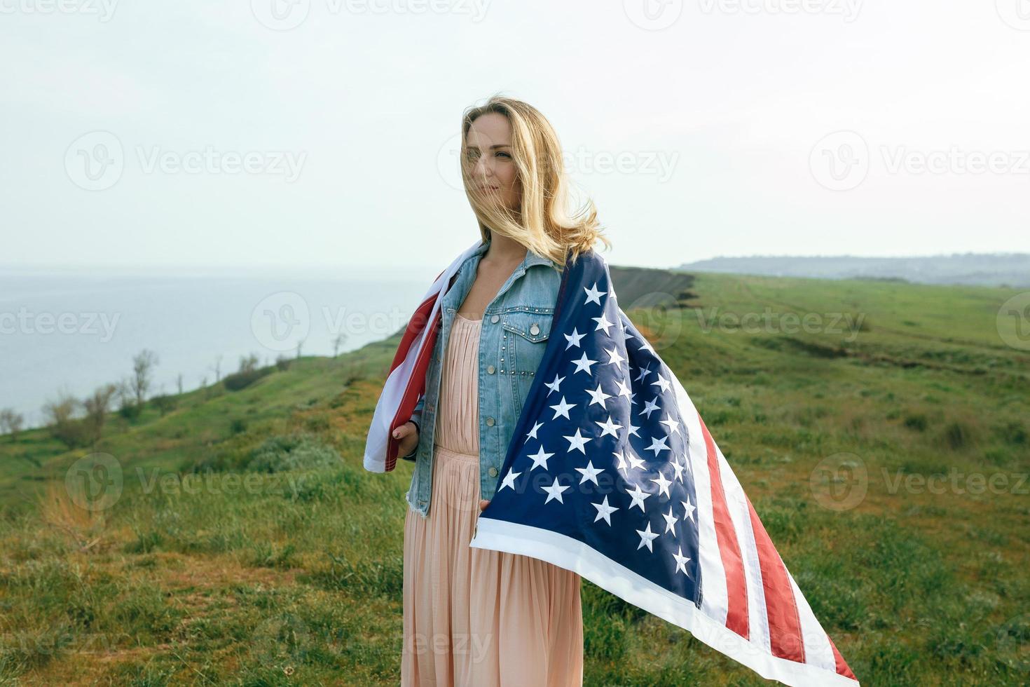 A girl in a coral dress and a denim jacket holds the flag of usa photo