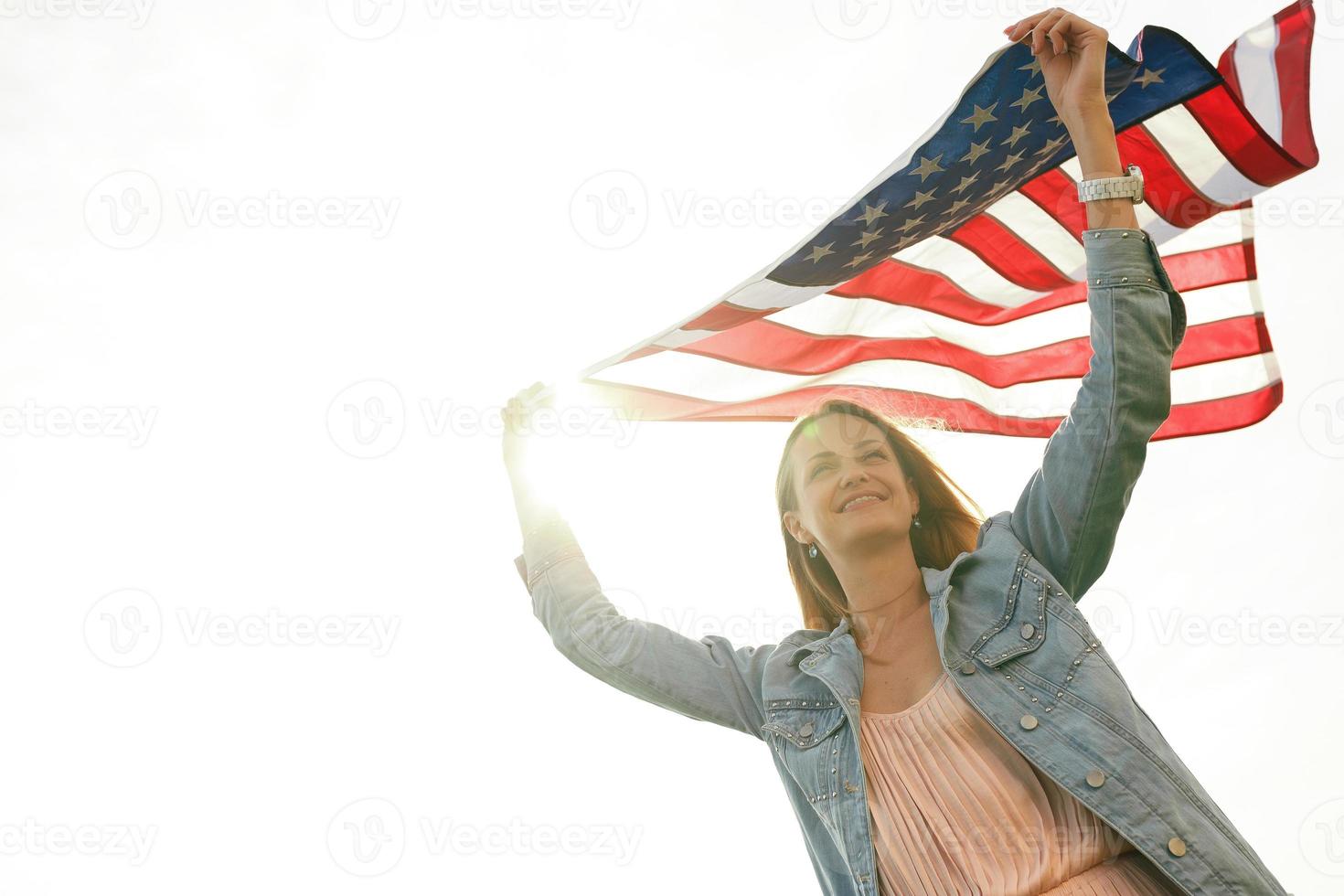 A girl in a coral dress and a denim jacket holds the flag of usa photo