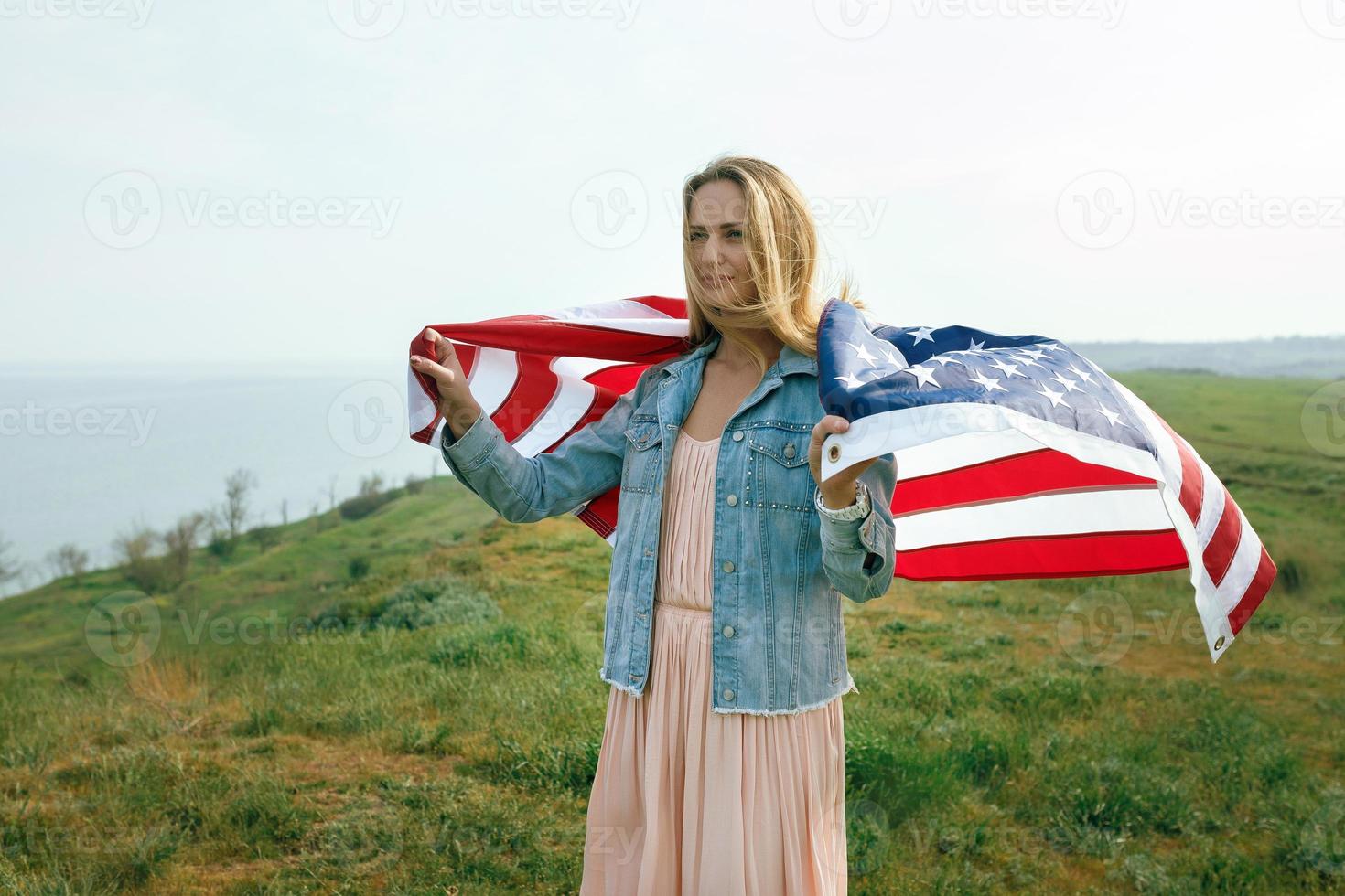 A girl in a coral dress and a denim jacket holds the flag of usa photo