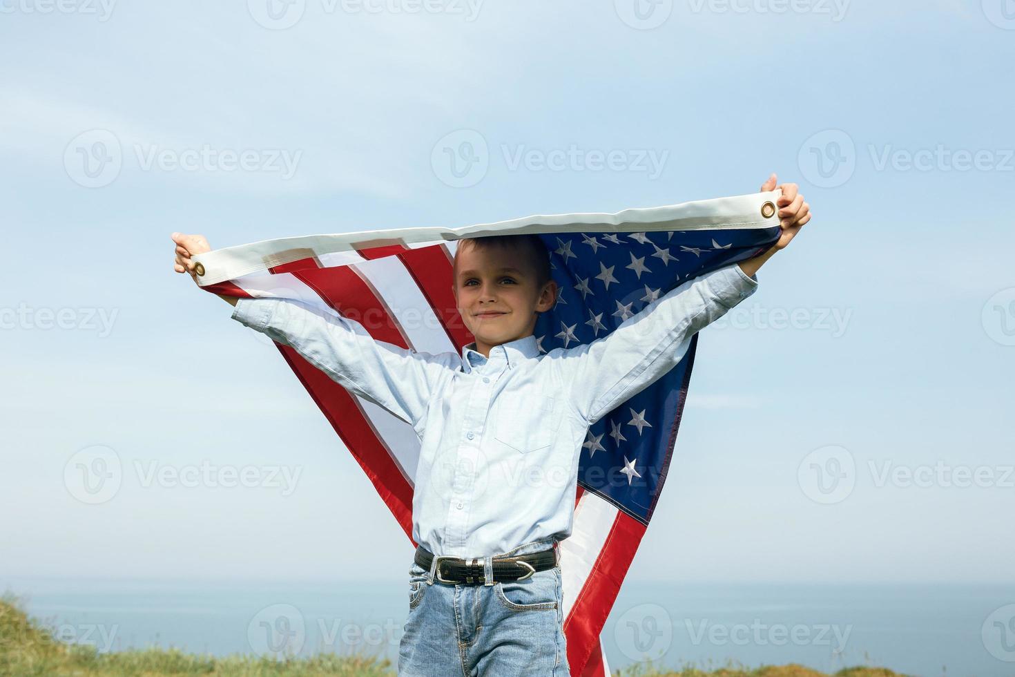 A little boy holds a flag of the United States against the sky photo