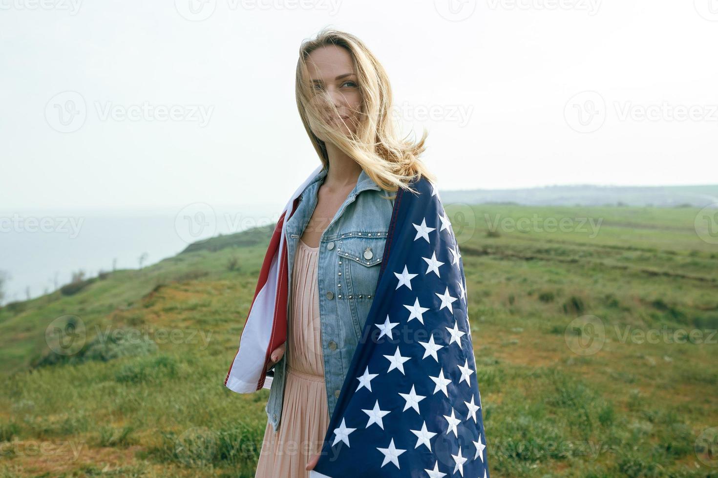 A girl in a coral dress and a denim jacket holds the flag of usa photo