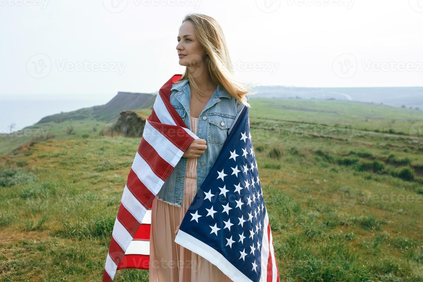 A girl in a coral dress and a denim jacket holds the flag of usa photo