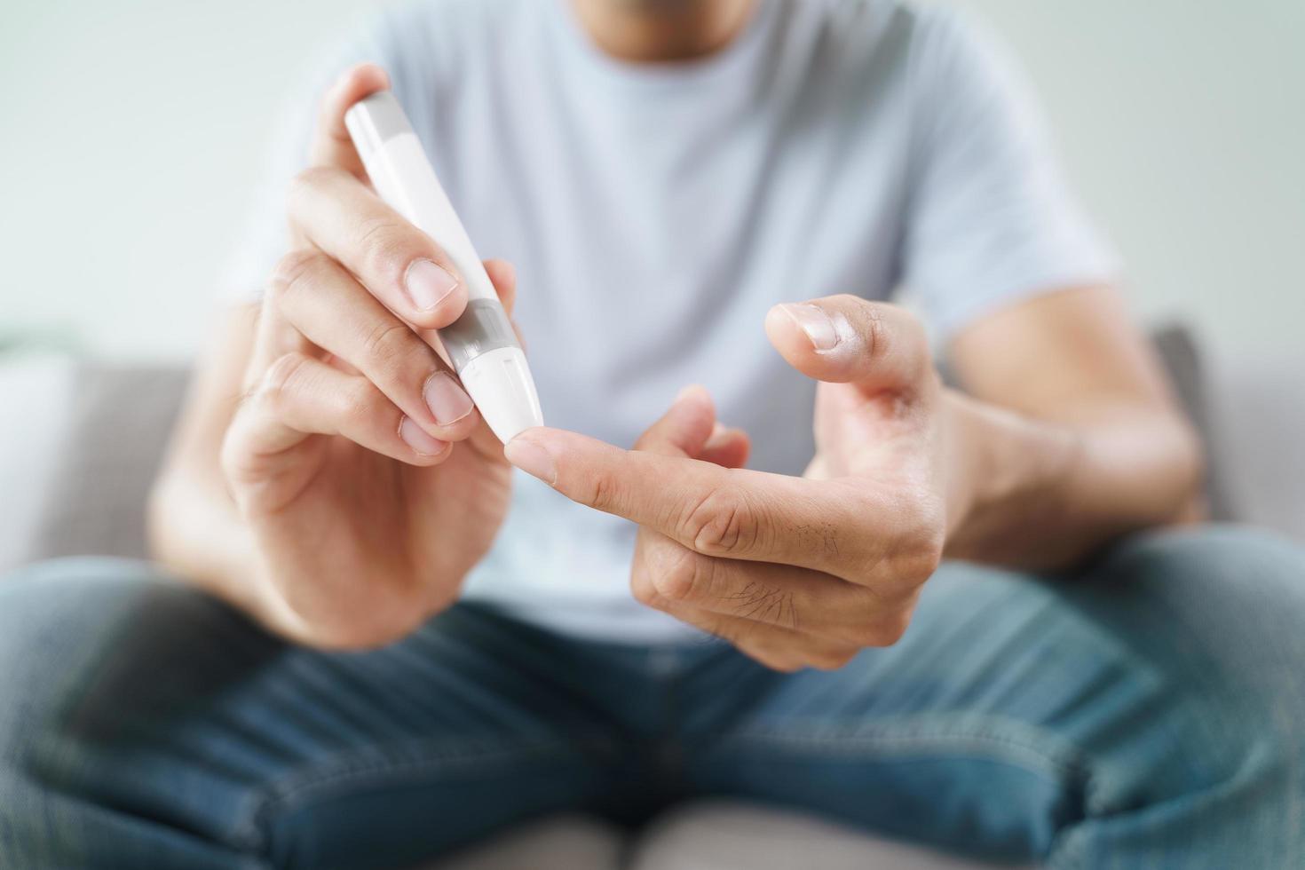 El hombre usa una lanceta en el dedo para controlar el nivel de azúcar en la sangre con un medidor de glucosa. foto
