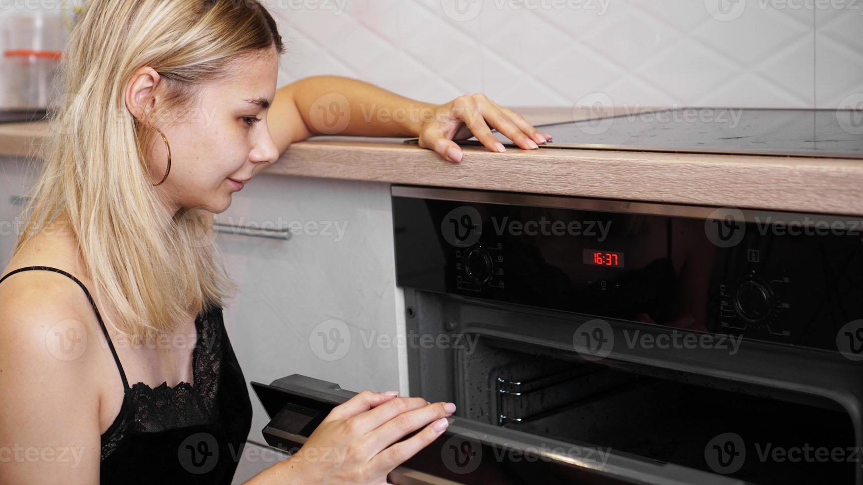 Mujer cocinando en la cocina abriendo la puerta del horno. foto