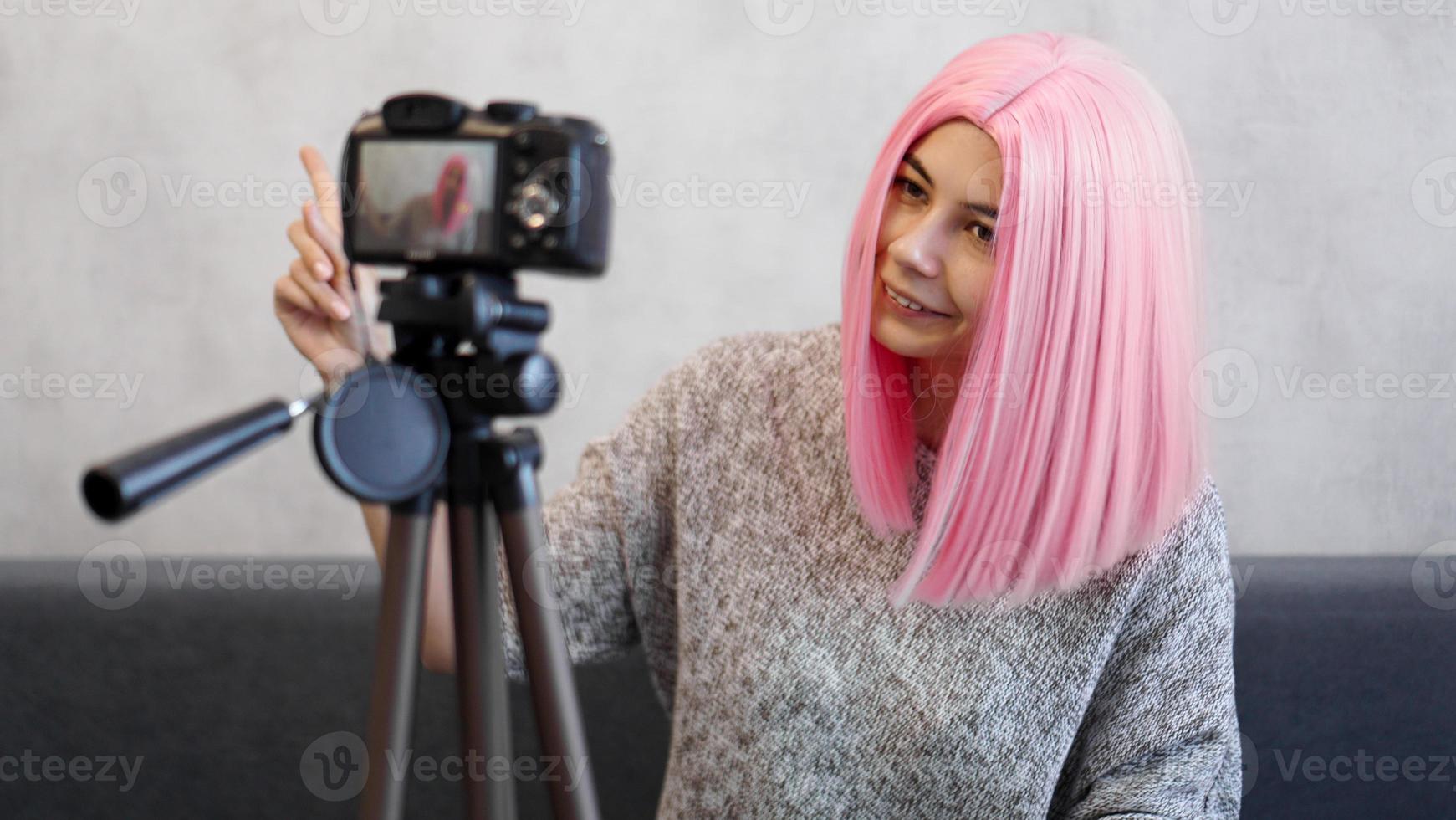 Happy girl blogger in pink wig in front of the camera on a tripod photo