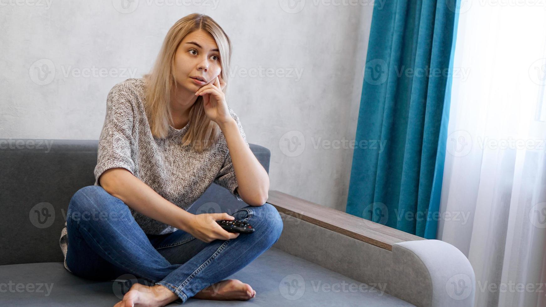 Young woman changing TV channels with remote control sitting on sofa photo