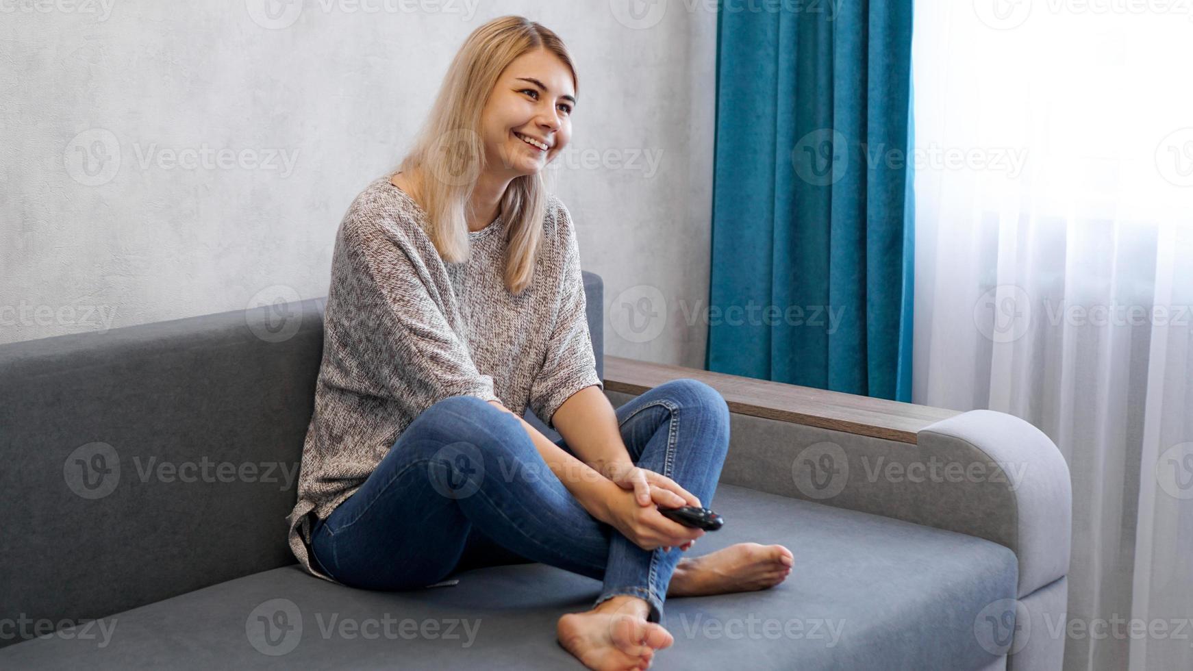 Mujer feliz viendo la televisión sentado en un sofá en el salón de casa foto