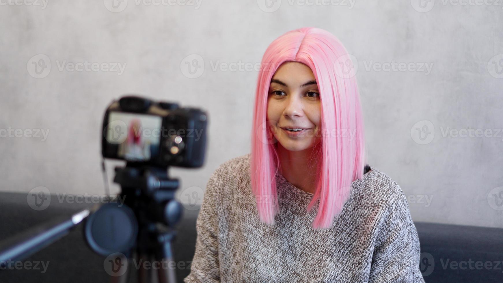 Happy blogger in pink wig in front of the camera on a tripod photo