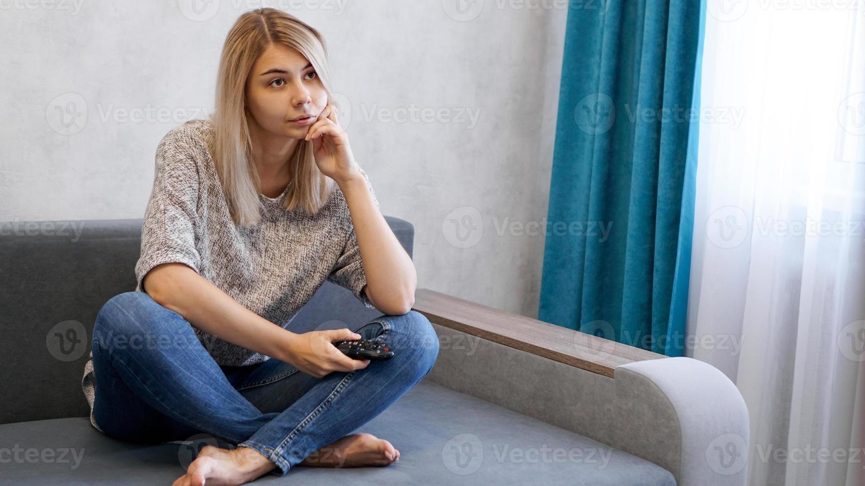 Una joven aburrida viendo la televisión con control remoto. foto
