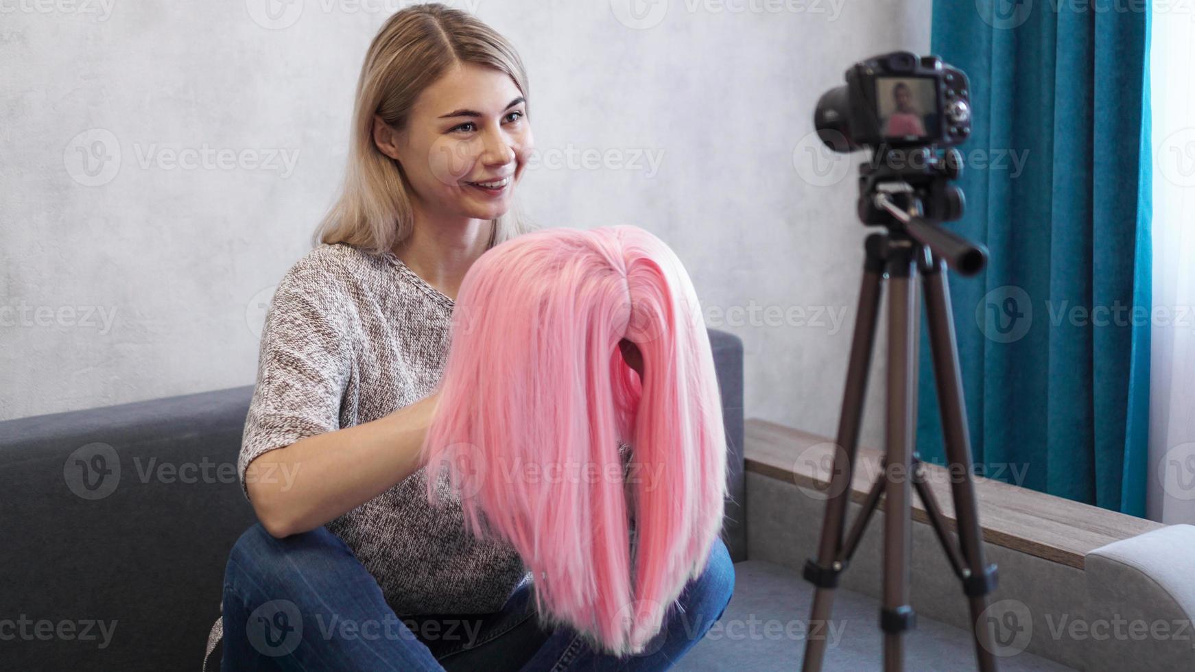 Woman blogger records video. She shows pink wig photo