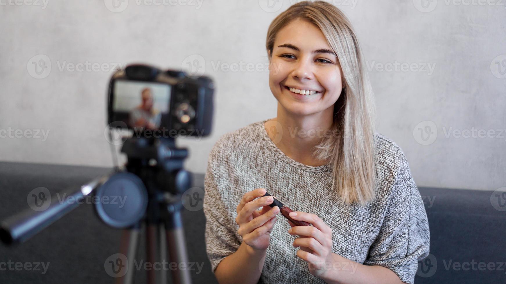 mujer vlogger mostrando lápiz labial. blogger de belleza en estudio casero foto