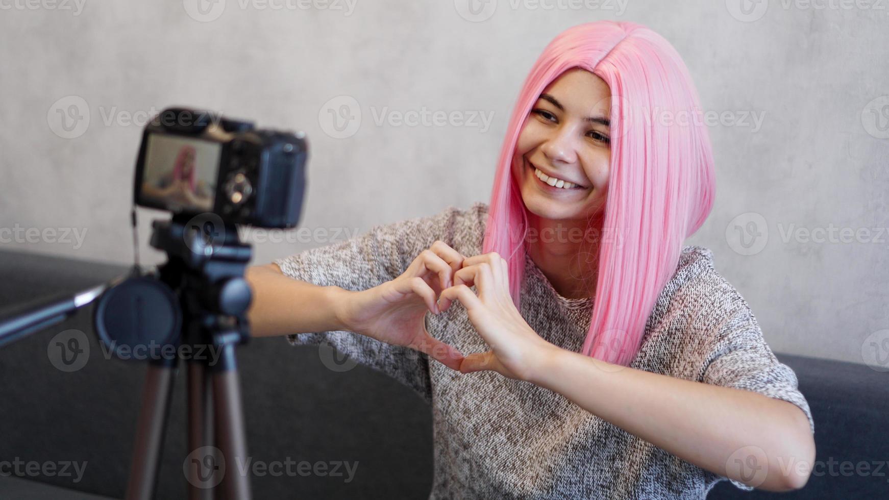 Woman looks at camera and shows heart shape sign. Girl with pink hair photo