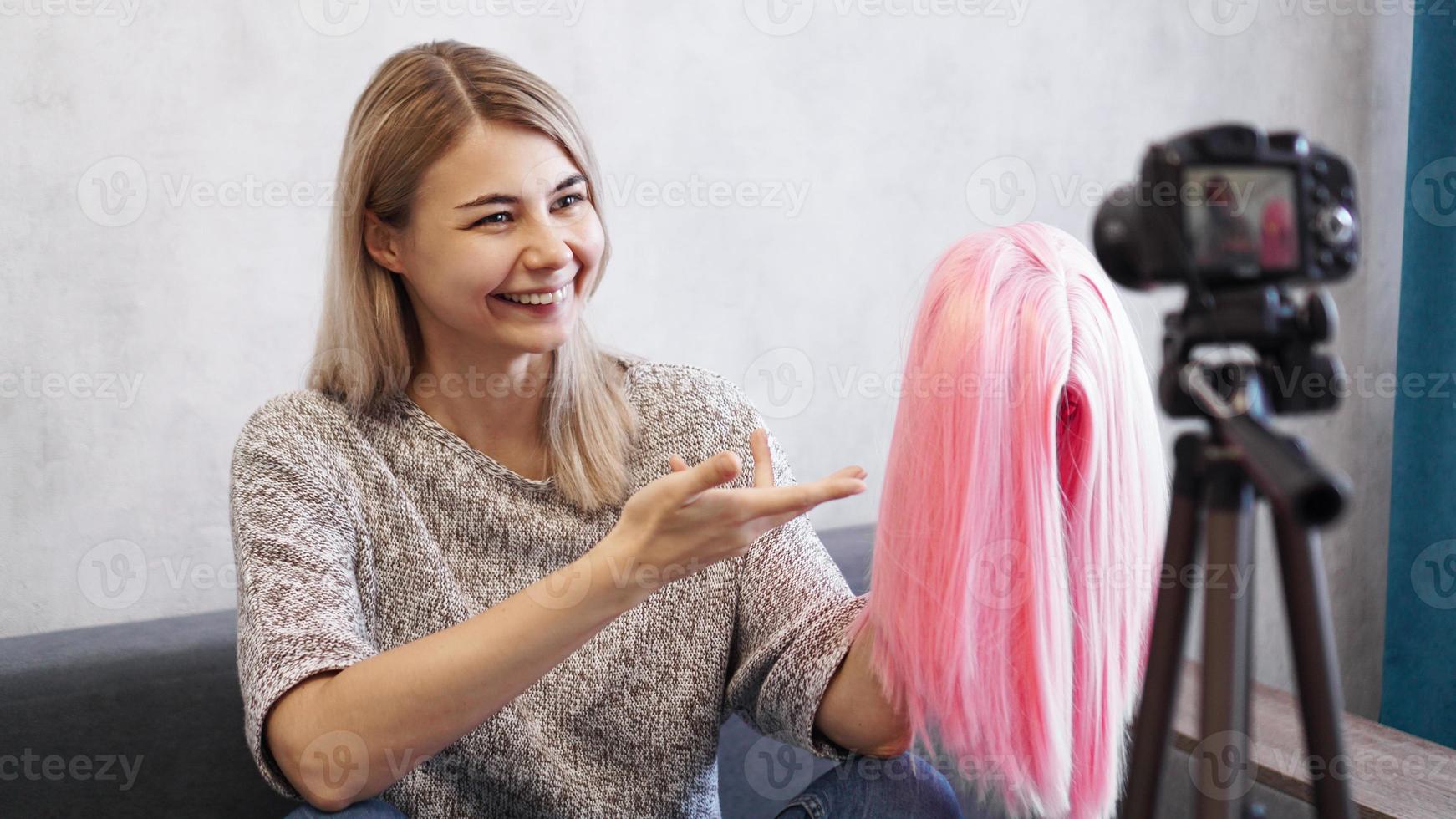 Woman blogger records video. She shows pink wig photo