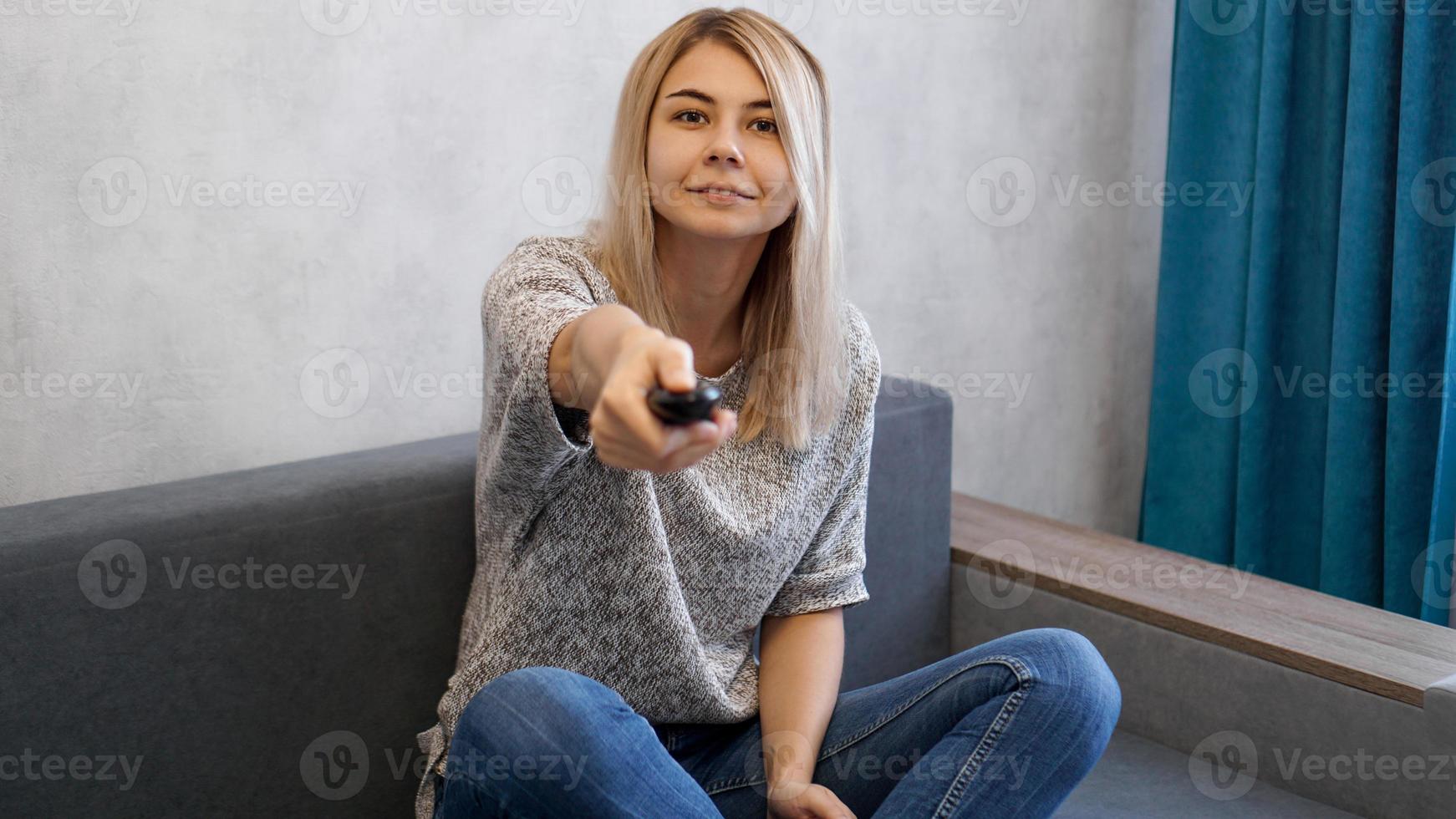 Young woman switches the television channels with the remote control photo