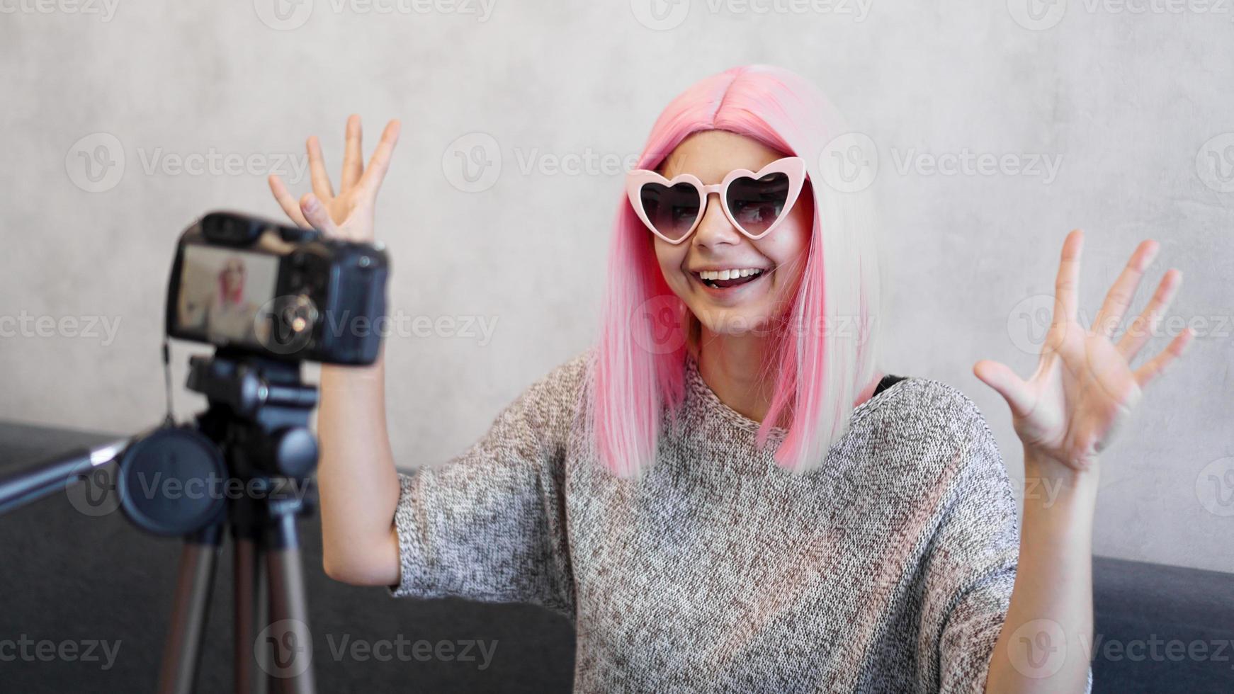 Happy girl blogger in pink wig in front of the camera on a tripod photo